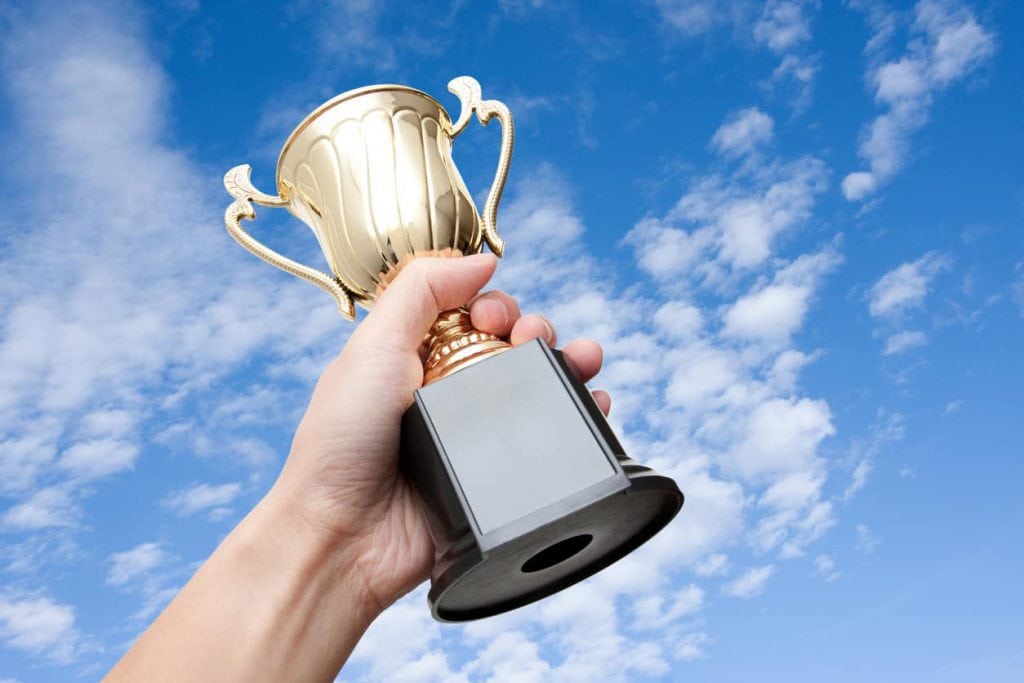 Close up of a hand holding a winners trophy against the sky.